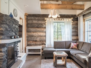 Una sala de estar acogedora con chimenea de piedra, un sofá, una mesita y una ventana con cortinas.