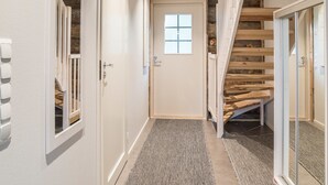Un couloir avec un escalier en bois, une porte dotée d’une fenêtre et un revêtement de sol texturé.