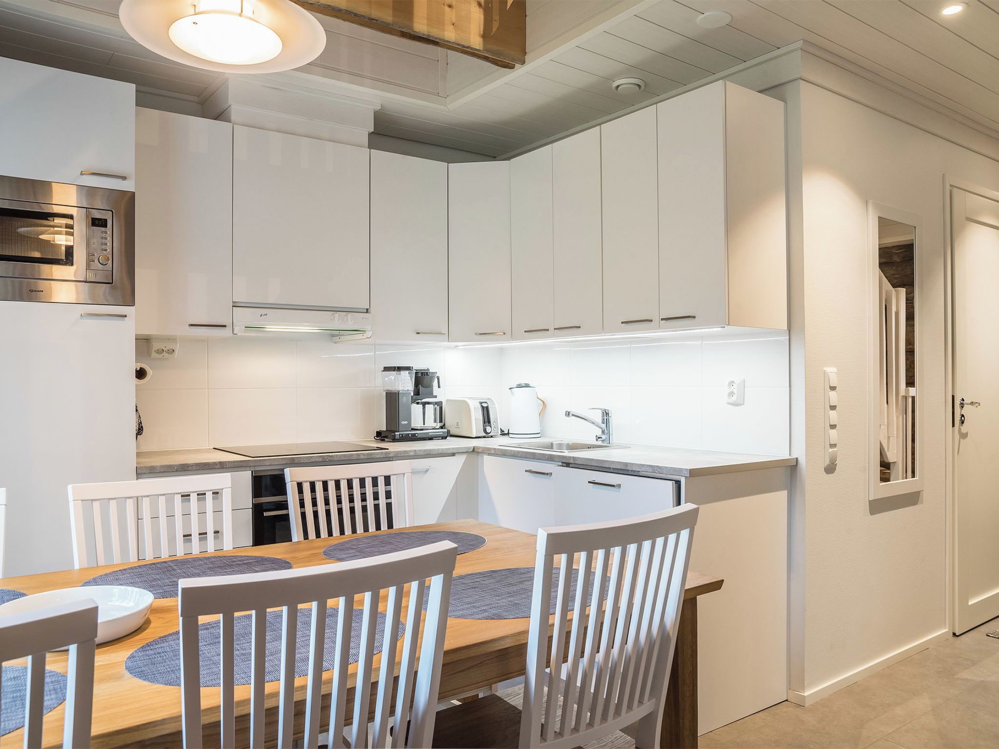 A modern kitchen with white cabinetry, a built-in oven, and a dining area with a wooden table and chairs.