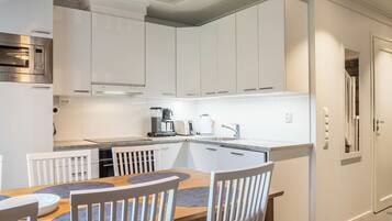 A modern kitchen with white cabinetry, a built-in oven, and a dining area with a wooden table and chairs.