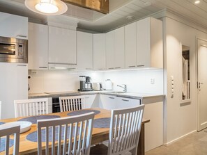 Una cocina moderna con armarios blancos, horno empotrado y comedor con mesa y sillas de madera.