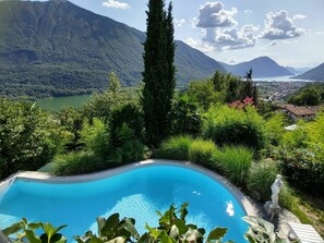 En swimmingpool omgivet af frodig vegetation og bjerge i baggrunden.