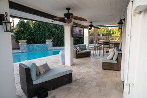 Un espacio al aire libre cubierto con piscina, mobiliario de mimbre y ventiladores de techo.