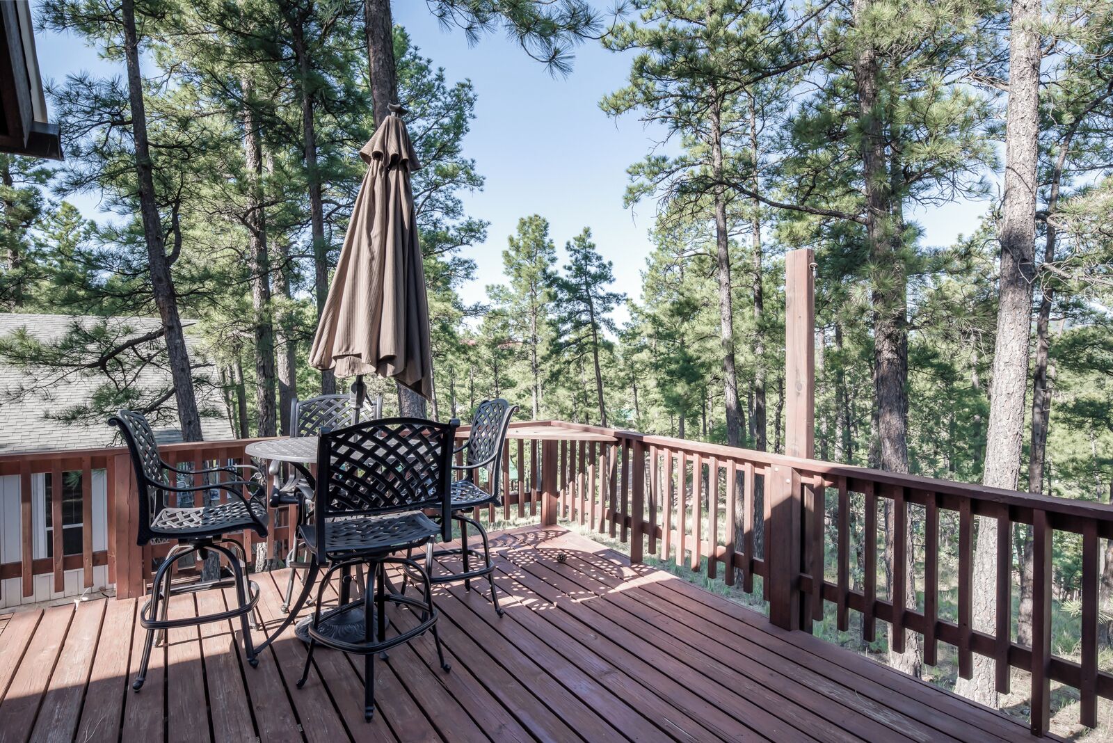 A wooden deck with a table and chairs, surrounded by tall pine trees.