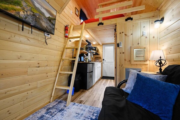 A cozy cabin interior with a wooden interior, a bunk bed, a kitchen area, and a small living space with a couch and a lamp.
