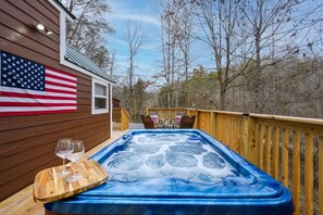 A hot tub on a wooden deck with an American flag, surrounded by trees.
