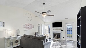 A living room with a gray sofa, a ceiling fan, a fireplace, and a large TV. - Cozy Home for Entire Family (Charlotte)