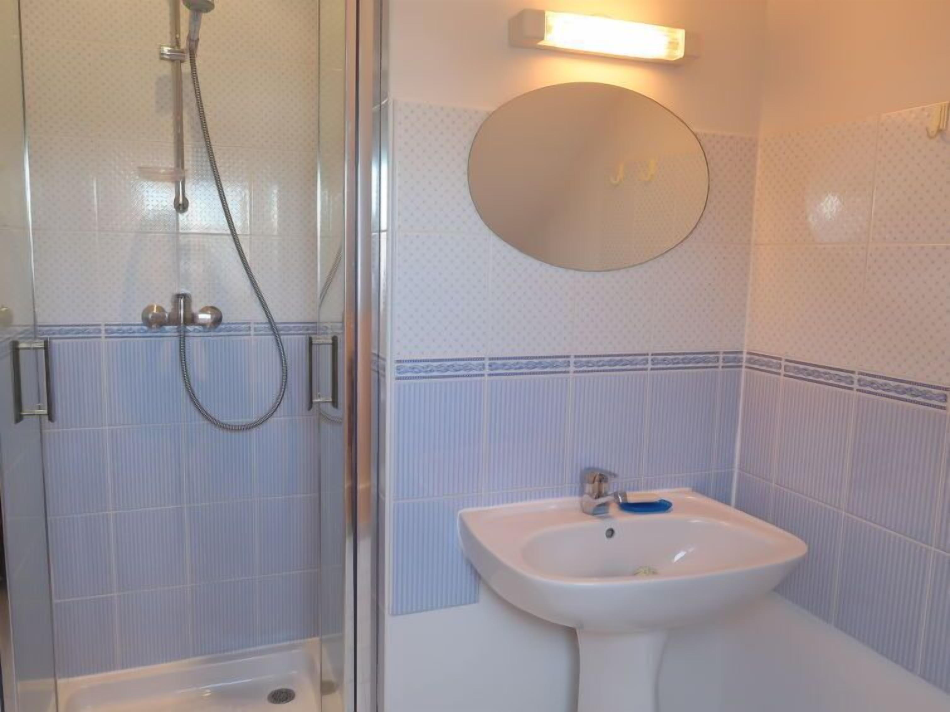 A bathroom with a glass-enclosed shower, a sink with a mirror above it, and patterned tiles.