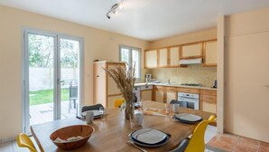 A modern kitchen with wooden cabinets, a dining table set for four, and a large window overlooking a garden. - Vacation home Lana by Interhome (Denneville)