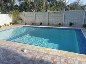A rectangular swimming pool with a tiled edge and a stone-tiled deck surrounding it.