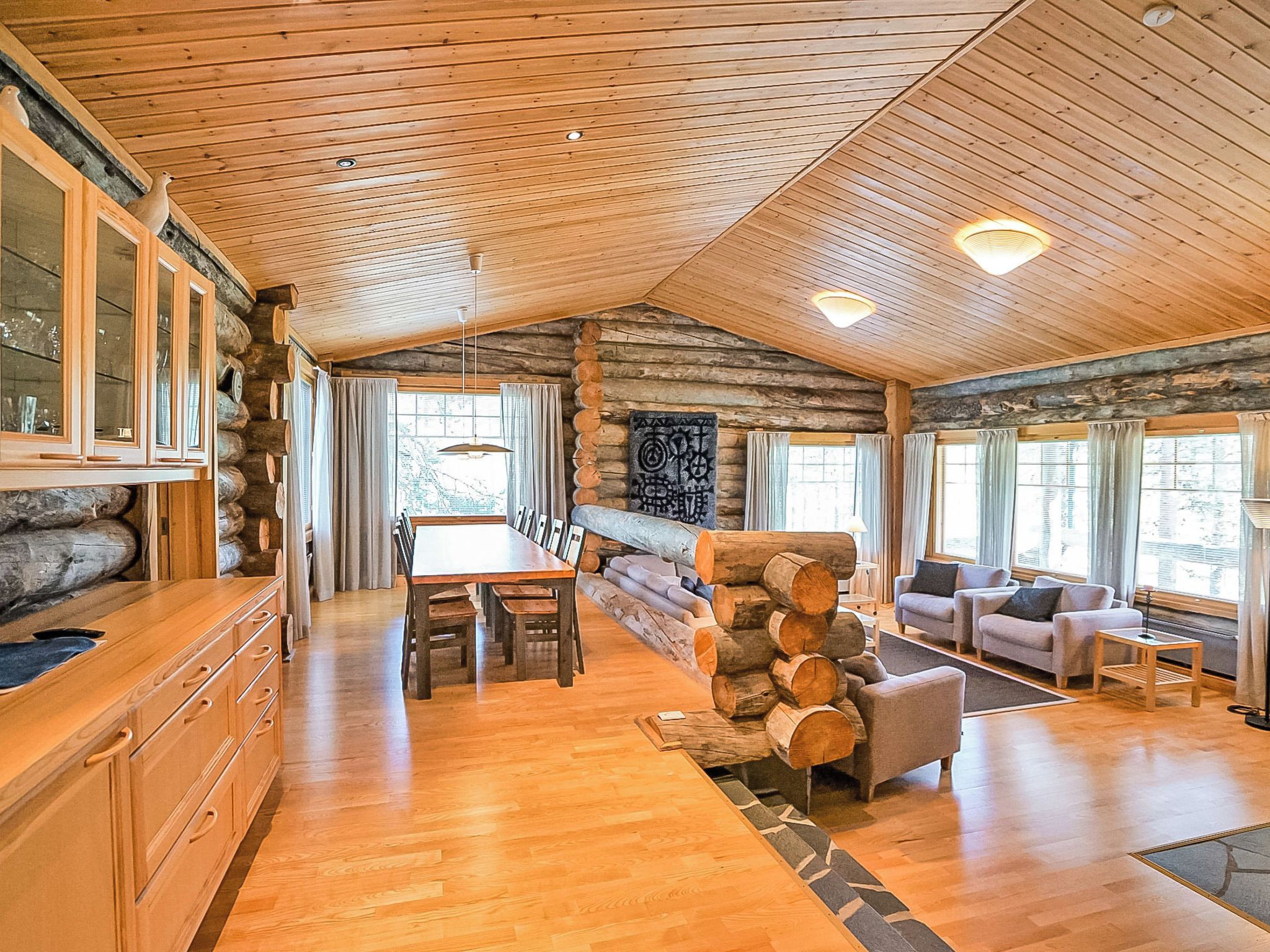 A spacious log cabin interior with a dining area, sofas, and a fireplace.