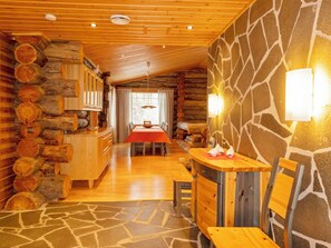 Interior de una cabaña de troncos con pared de piedra, mobiliario de madera y comedor.