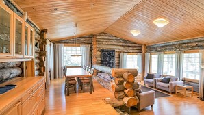 Ein Holzblockhaus-Interieur mit einem Holzesstisch, Stühlen, einer Couch und einem Kamin.