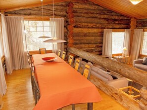 A log cabin interior with a dining table, chairs, a sofa, and a window with curtains.