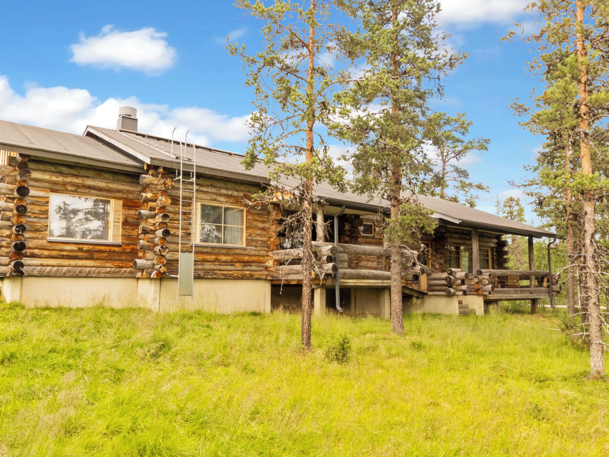 A log cabin with a porch and a chimney, surrounded by trees and grass.