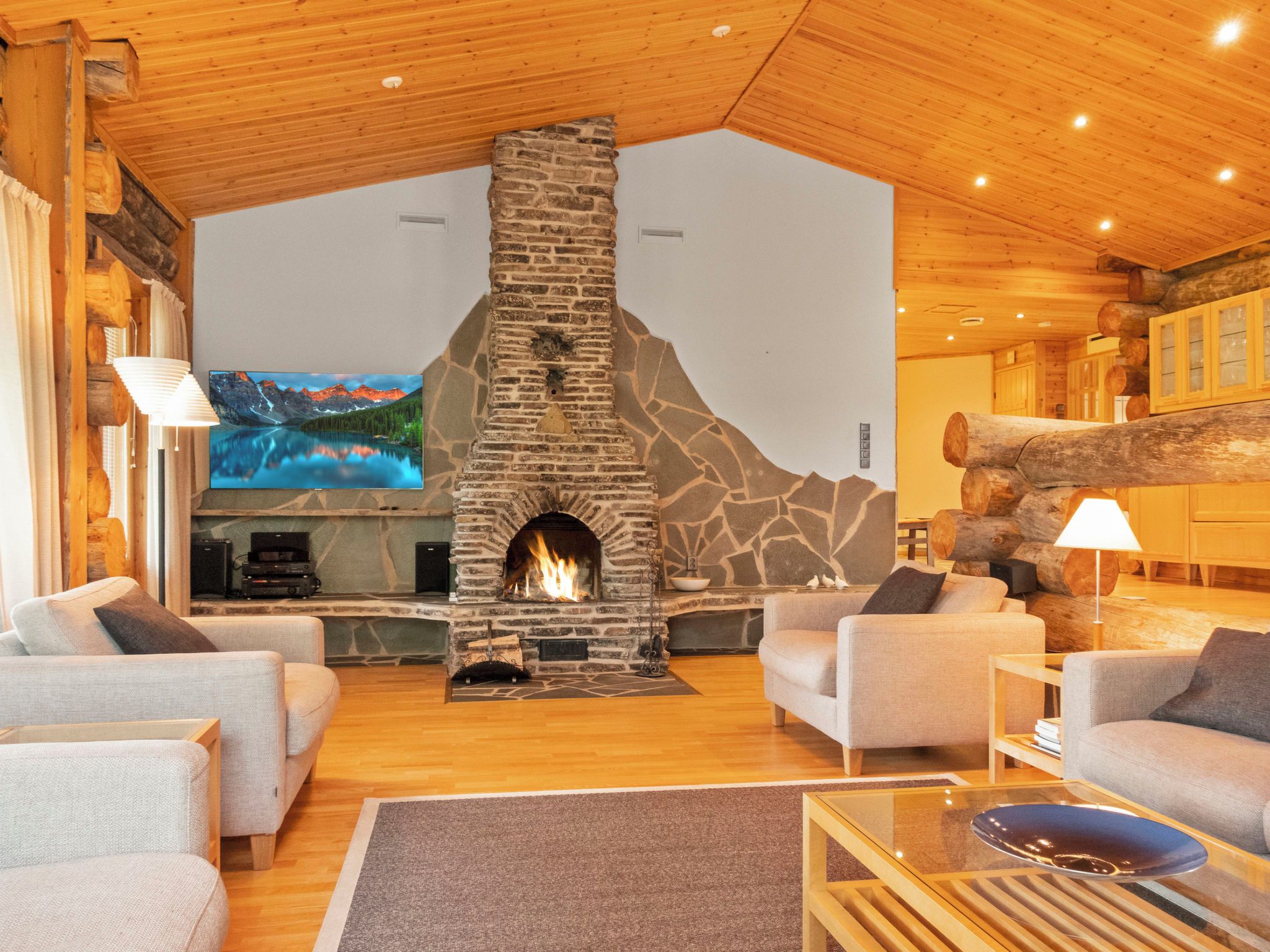 A cozy living room with a stone fireplace, comfortable seating, and a large TV screen.