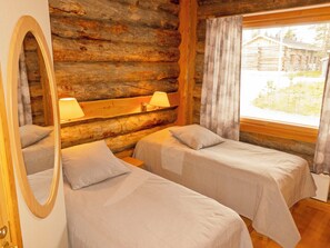 A log cabin room with two beds, a mirror, and a window with curtains.