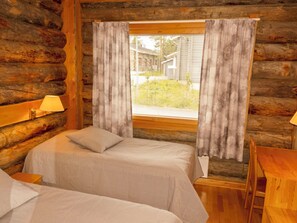 Una habitación de cabaña de troncos con dos camas, una ventana con cortinas, una lámpara y una mesa de madera.