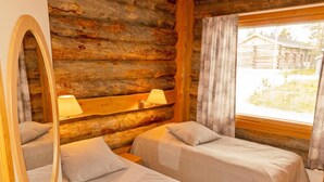 Ein Blockhauszimmer mit zwei Betten, einem Spiegel und einem Fenster mit Vorhängen.