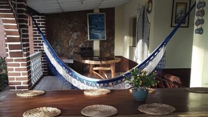 Een houten eettafel met geweven placematen, een hangmat en een potplant.