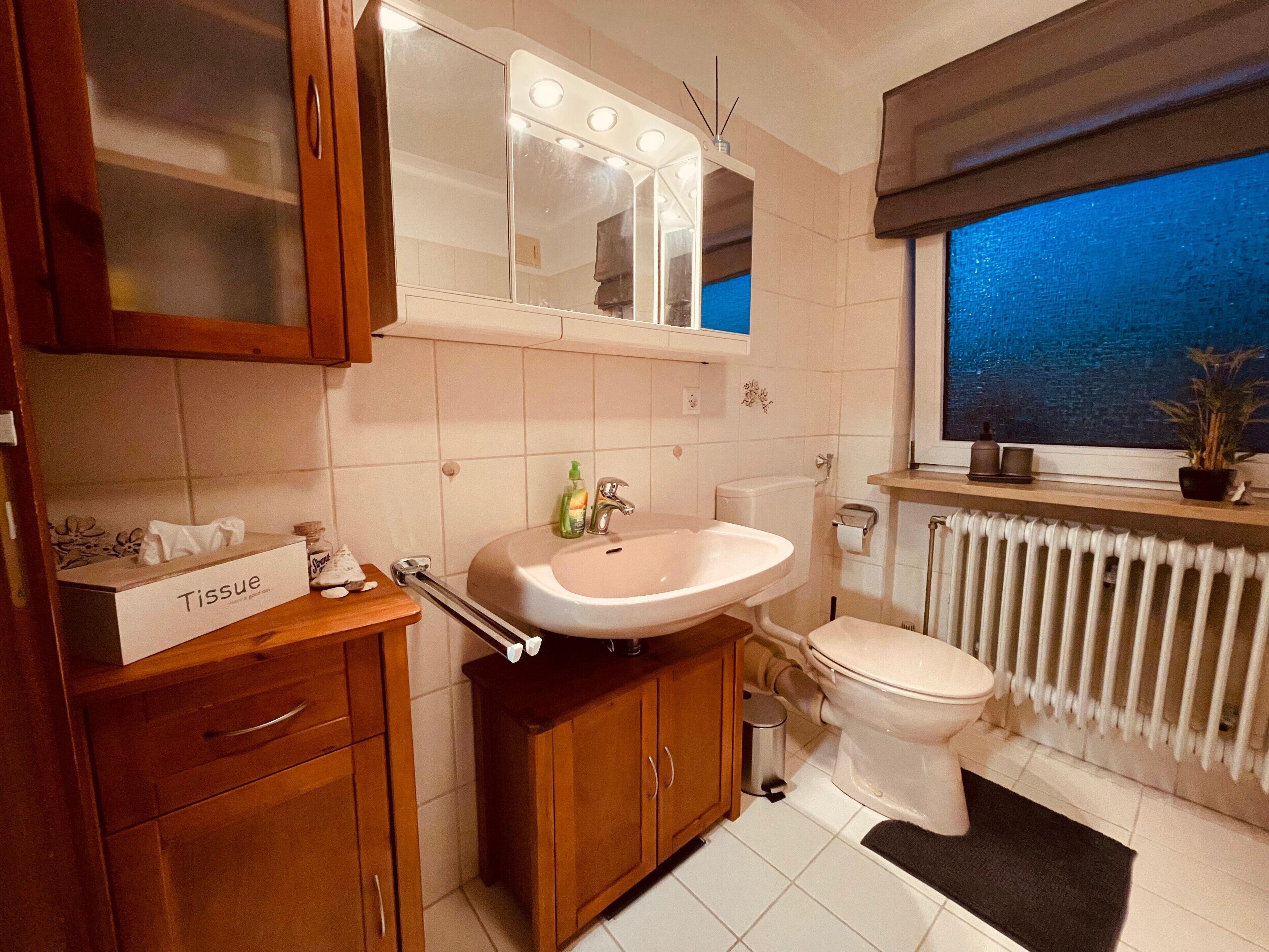 Un bagno con lavandino, WC, specchio e finestra.