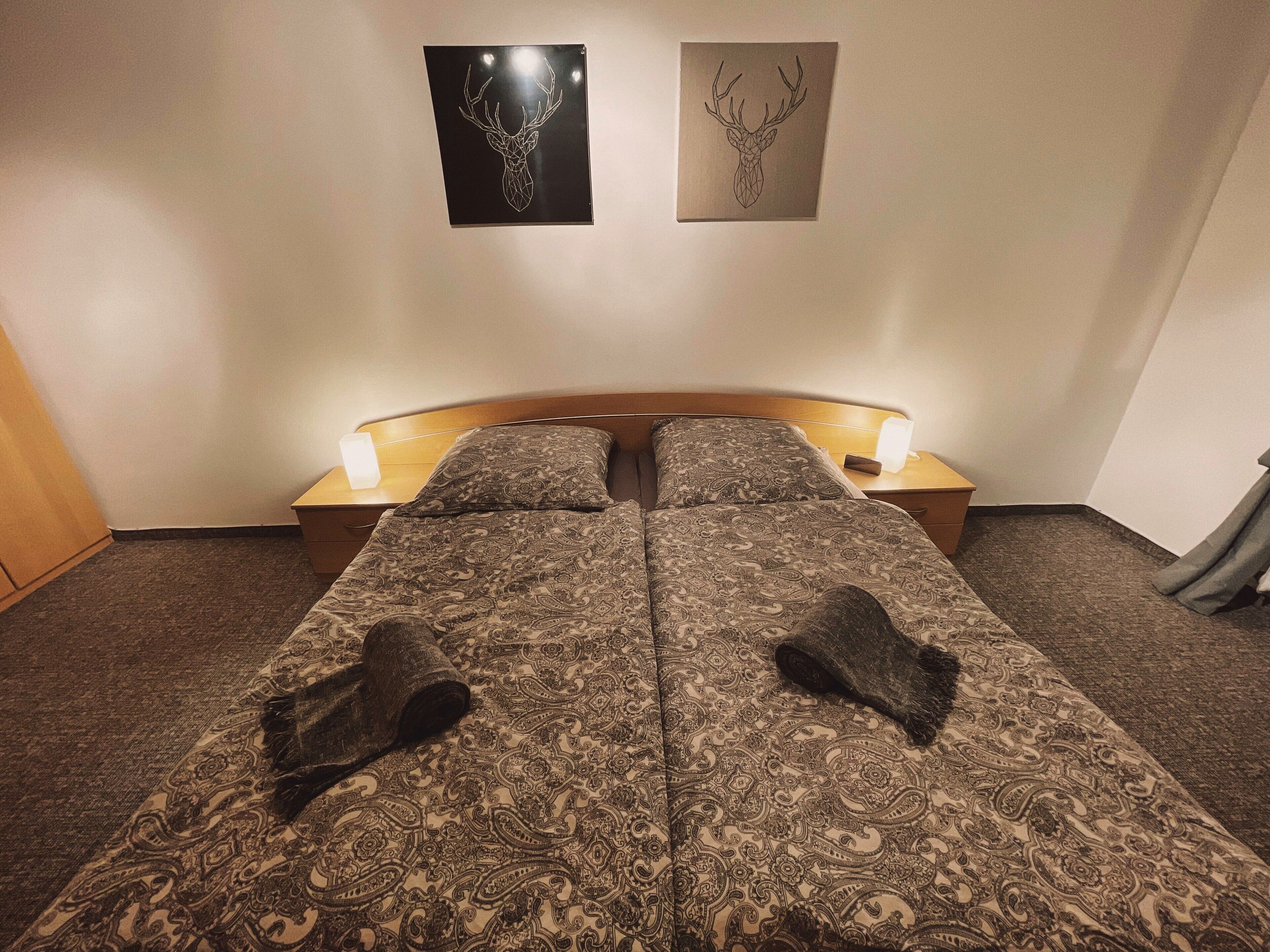 Una cama doble con ropa de cama estampada, dos lámparas de noche y dos obras de arte en la pared.
