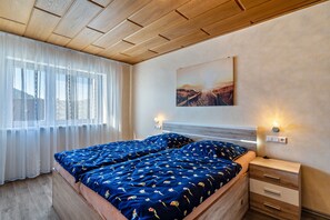 A bedroom with a wooden ceiling, a bed with blue floral bedding, a nightstand with a lamp, and a painting on the wall.