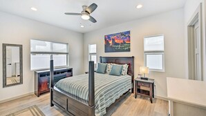 Una camera da letto con un letto, una ventola a soffitto, un comodino, una lampada, un quadro e una finestra.