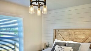Camera da letto con un letto a struttura in legno, una coperta bianca e un lampadario con tre luci.