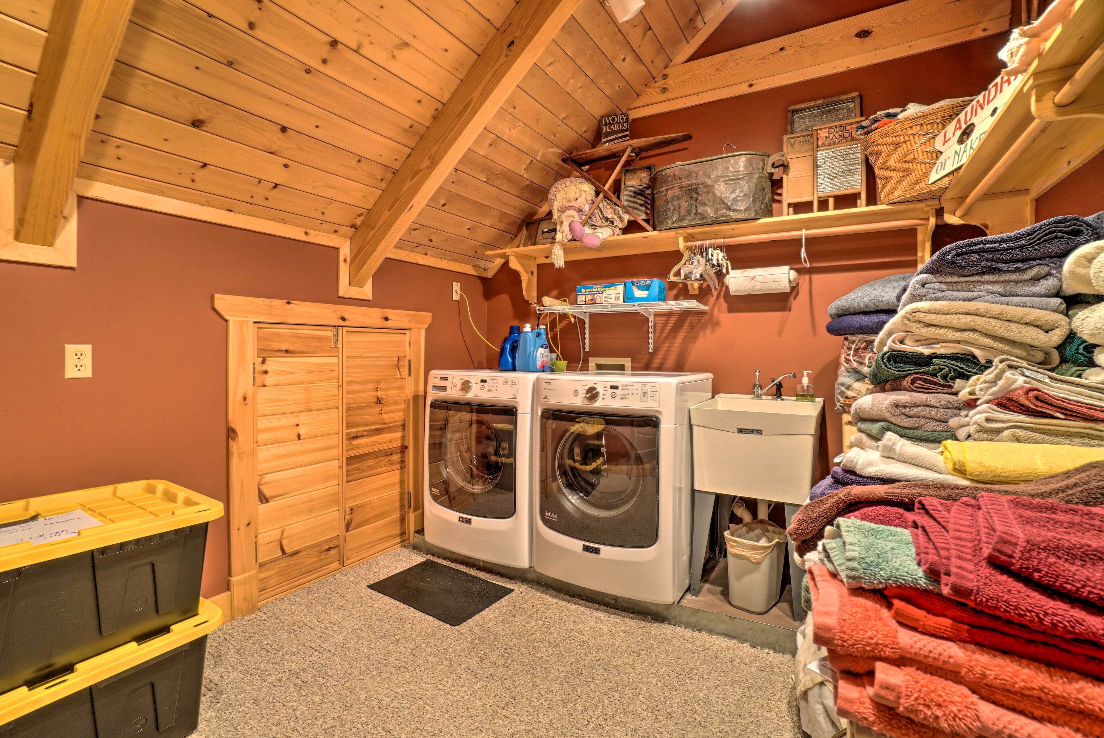 A laundry room with two front-loading washing machines, a sink, and a shelf with folded towels.
