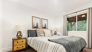 A bedroom with a bed, two bedside tables, a window with curtains, and two wall-mounted pictures. - Captivating and Charming Retreat, Game Rooms, Pool Table, Foosball, 20 Min to Portland (West Linn)