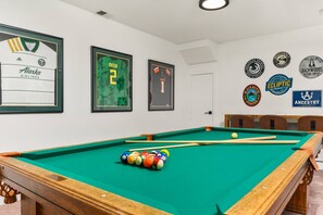 Uma mesa de bilhar com bolas, uma camisa emoldurada e diversos logotipos de cervejaria na parede.