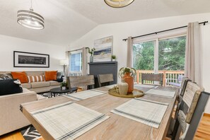 A dining area with a wooden table, chairs, and a view of the outdoors through large windows. - Captivating and Charming Retreat, Game Rooms, Pool Table, Foosball, 20 Min to Portland (West Linn)