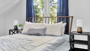 A bedroom with a bed, a window with curtains, a bedside table with a lamp, and a small plant. - Esser · 4Bed Charmer in Central Washington/East Peoria (Washington)