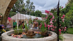 A garden with a fountain, a white tent, and a metal fence.