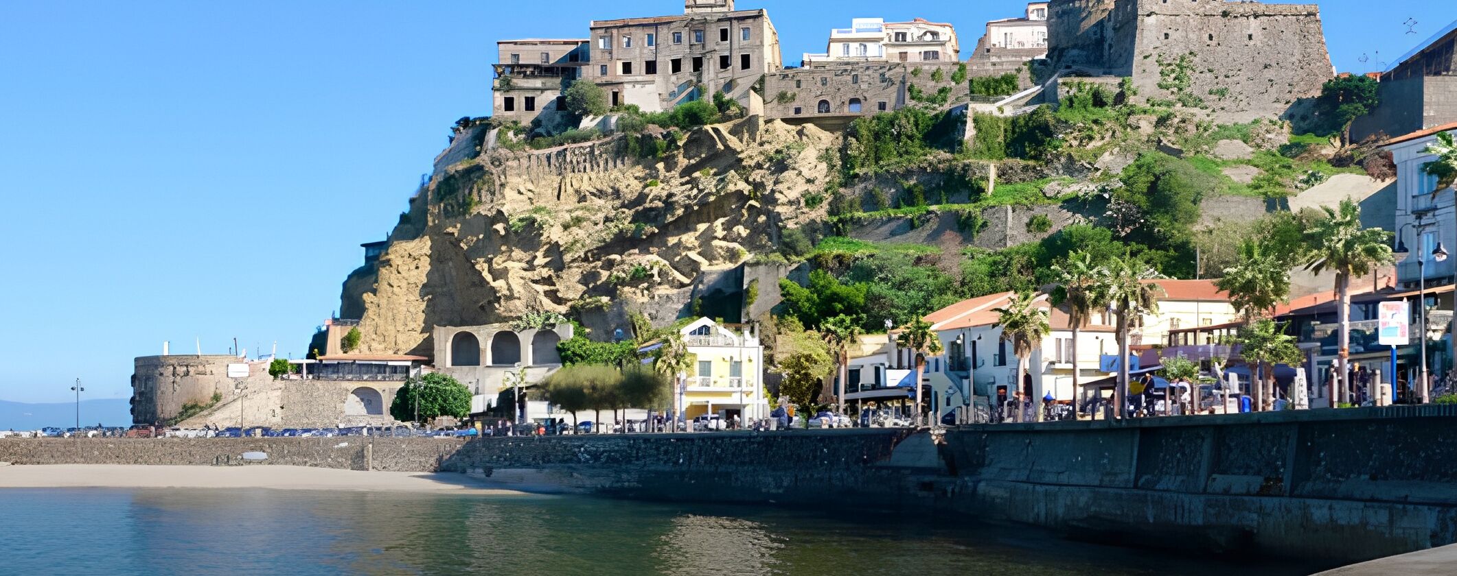 A coastal town with a historic castle on a cliff, a promenade, and a beach.