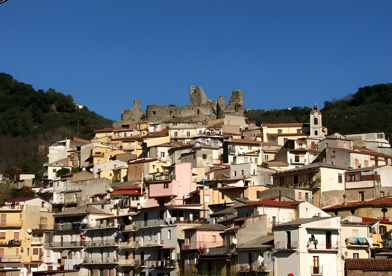 A densely packed hillside town with historic ruins and a church tower.