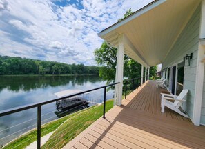 Une terrasse en bois avec des chaises blanches, un espace abrité et une vue sur un lac.