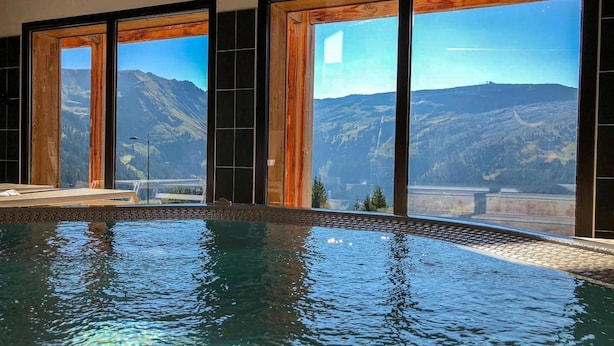 An indoor swimming pool with a view of mountains through large windows. - South-facing panoramic mountain view - T2 ski in, Pool & Spa (FLAINE, Arâches-la-Frasse)