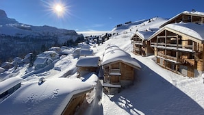 A snow-covered mountain village with wooden buildings, including a chalet with balconies, set against a backdrop of snow-capped peaks and a clear blue sky. - South-facing panoramic mountain view - T2 ski in, Pool & Spa (FLAINE, Arâches-la-Frasse)