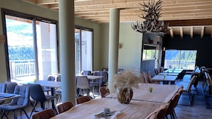 A spacious dining area with a large wooden table, comfortable seating, and a view of the outdoors. - South-facing panoramic mountain view - T2 ski in, Pool & Spa (FLAINE, Arâches-la-Frasse)