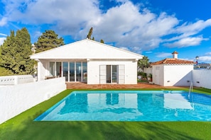 Een witte villa met zwembad, terras en uitzicht op zee.