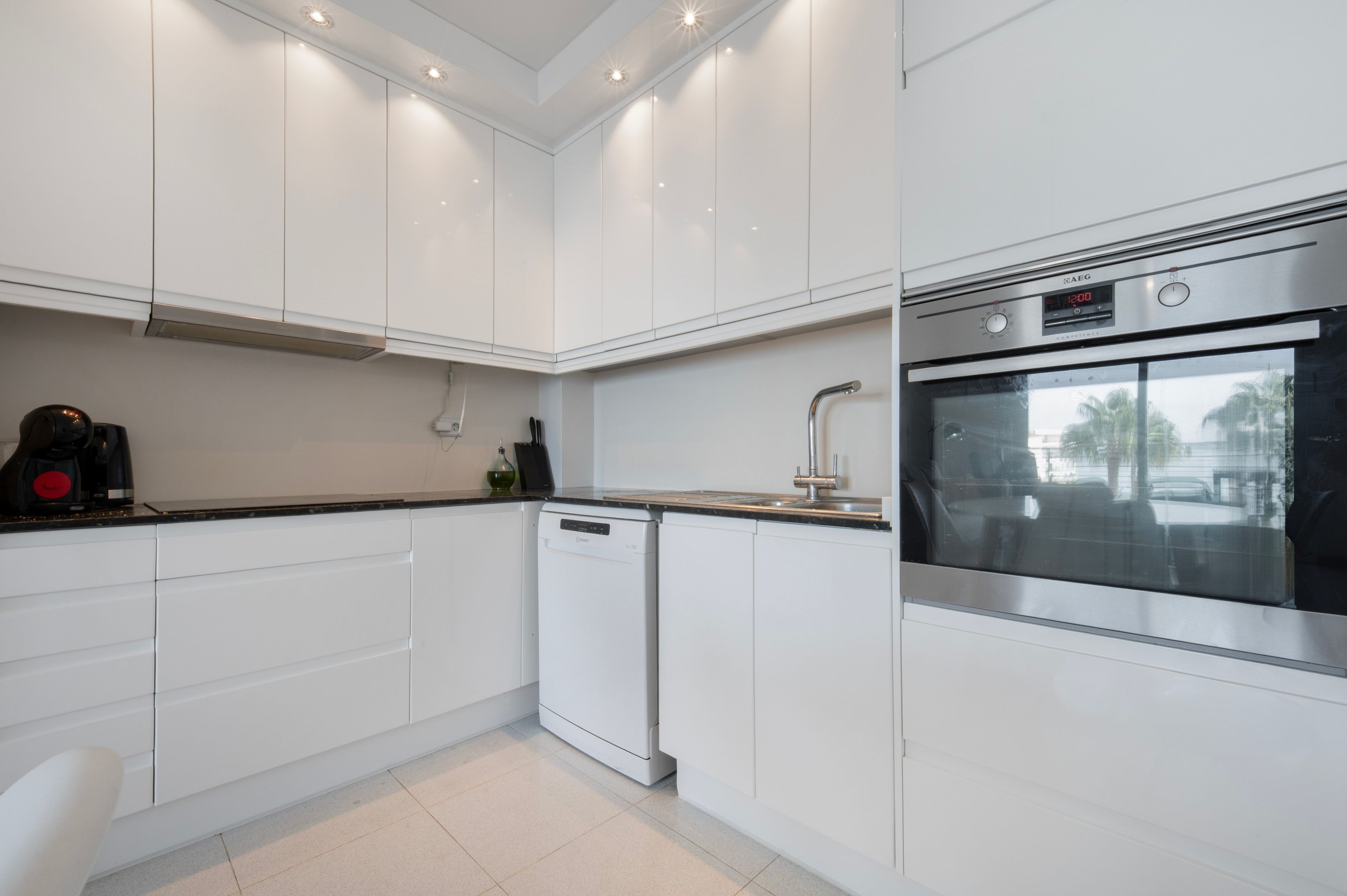 A modern kitchen with white cabinetry, a dishwasher, a stainless steel oven, and a coffee maker.