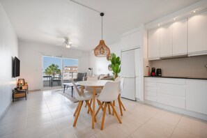 A modern kitchen with white cabinetry, a dining table with chairs, a ceiling fan, and a view to the outside. - Apartment "Costabella Altea" with Mountain View, Pool, Wi-Fi, Garden & Terrace (Altea)