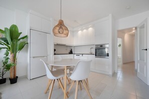 A modern kitchen with white cabinetry, a central island, and a dining area with white chairs. - Apartment "Costabella Altea" with Mountain View, Pool, Wi-Fi, Garden & Terrace (Altea)
