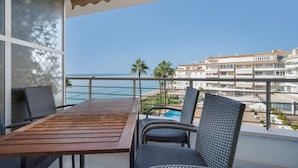 A balcony with a wooden table and wicker chairs, overlooking a beach and a resort area. - Apartment "Costabella Altea" with Mountain View, Pool, Wi-Fi, Garden & Terrace (Altea)