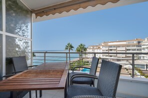 A balcony with a wooden table and wicker chairs, overlooking a beach and a resort area. - Apartment "Costabella Altea" with Mountain View, Pool, Wi-Fi, Garden & Terrace (Altea)