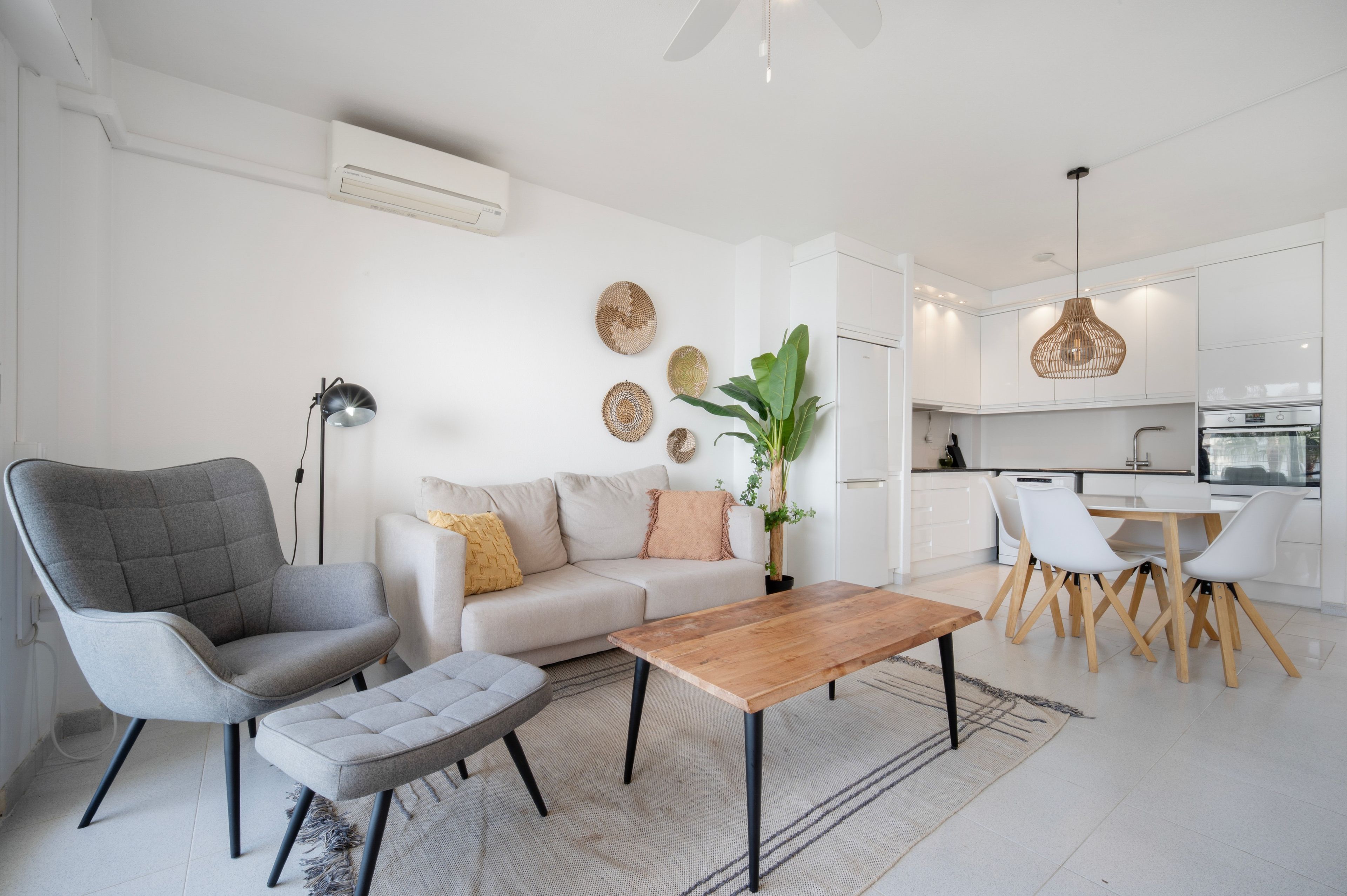 A modern living room with a grey sofa, a wooden coffee table, and a dining area with white chairs.