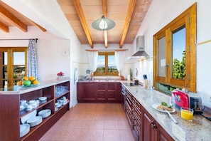 A kitchen with wooden cabinets, a granite countertop, a red toaster, and a view through the window.