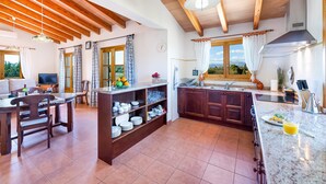 A spacious kitchen with wooden beams, a dining area with a table and chairs, and a view through the window. - Villa Son Allarga with Pool, Wi-Fi & Terrace (Costitx)